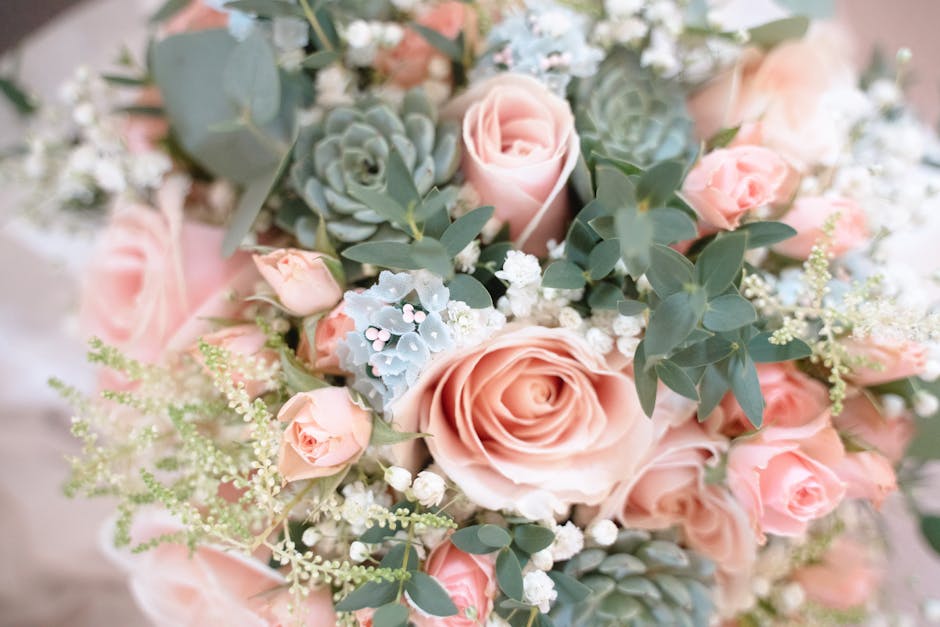 A floral arrangement featuring a bouquet of soft pink roses, complemented by small white baby's breath and blue-gray succulents. The bouquet also contains eucalyptus leaves with silvery-green foliage,