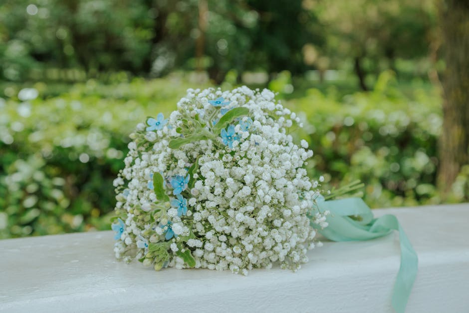 A floral bouquet featuring a dense cluster of white baby's breath flowers with small, delicate petals, complemented by light blue blossoms with five petals each. The bouquet is arranged in a rounded, 